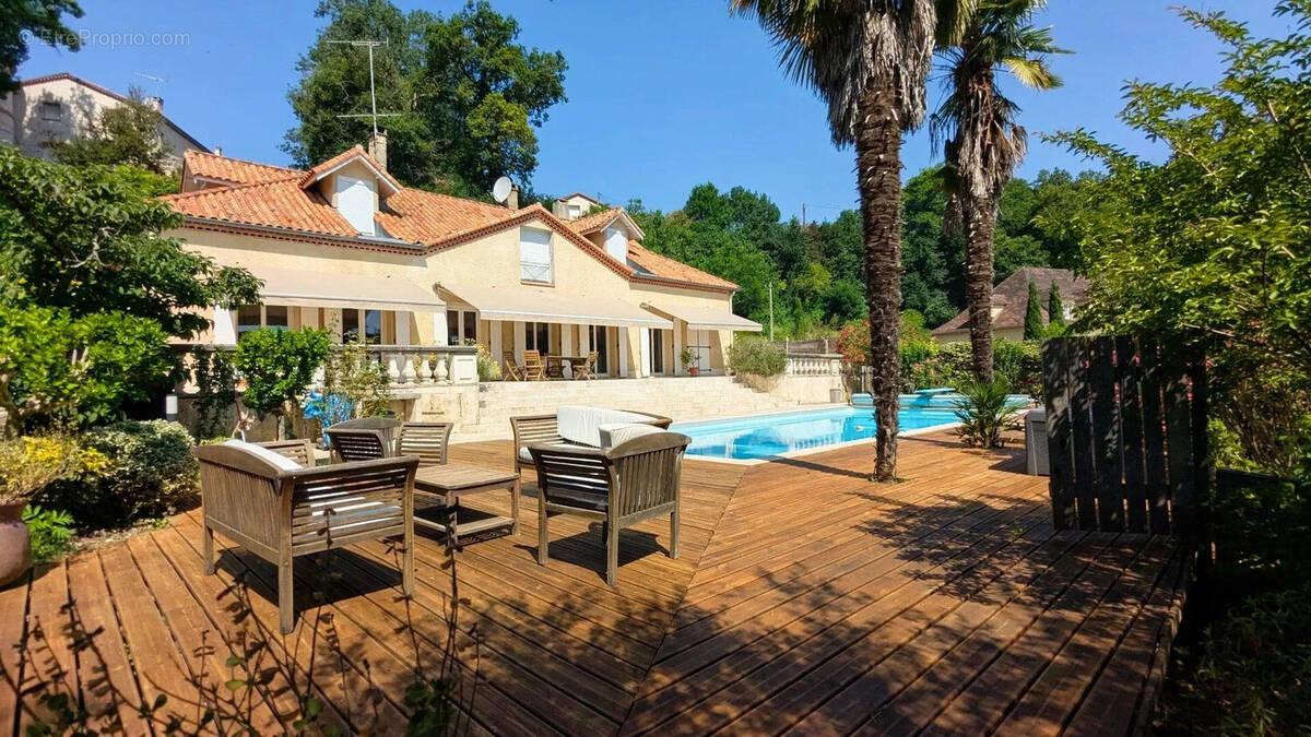 Une belle maison avec une terrasse en bois, des palmiers et une piscine, entourée de verdure. - Maison à FOULAYRONNES