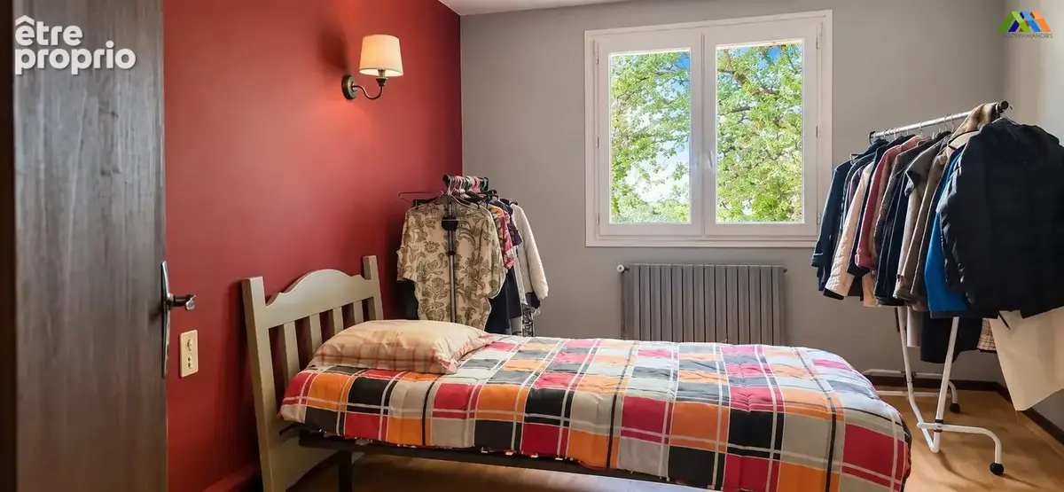 Bedroom with a red feature wall, single bed and views of leafy trees.