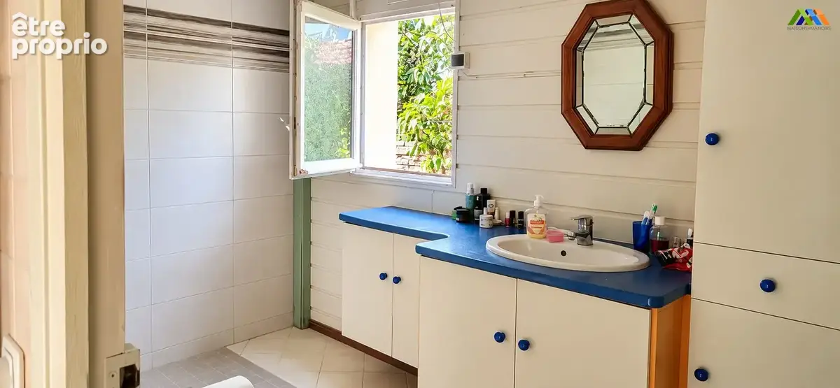Salle d'eau avec douche carrelée, meuble vasque blanc et plan bleu, éclairée par une fenêtre